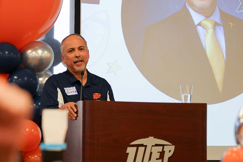 Two attendees pose together at a banquet table during a UTEP Engineering homecoming gathering, seated among other guests with event decorations, plates, beverages, and table settings visible throughout the room.